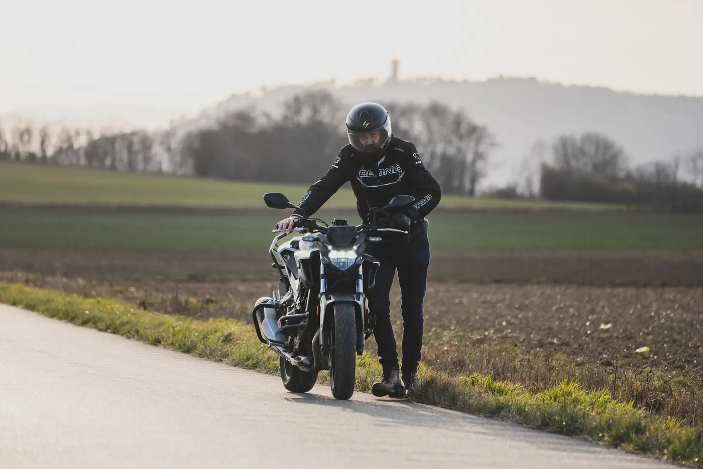 Rider pausing beside a motorcycle on a tropical road
